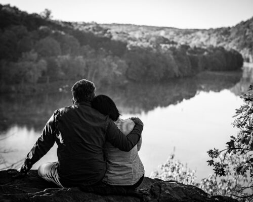 man in black and white striped long sleeve shirt sitting on rock near lake